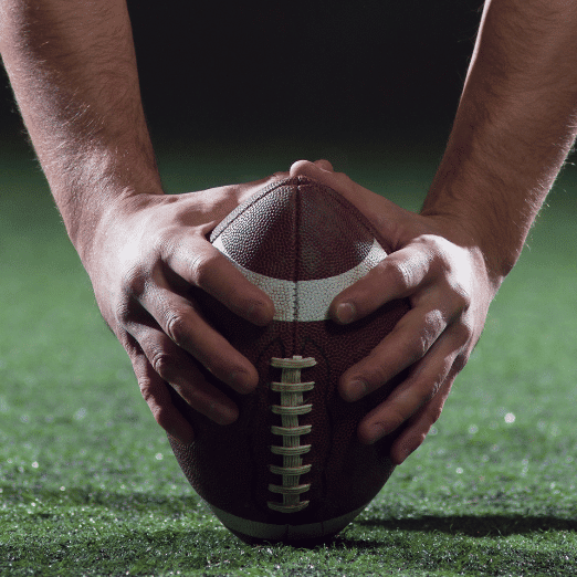 Stylized photo of a player holding a football and preparing to snap it to the quarterback.
