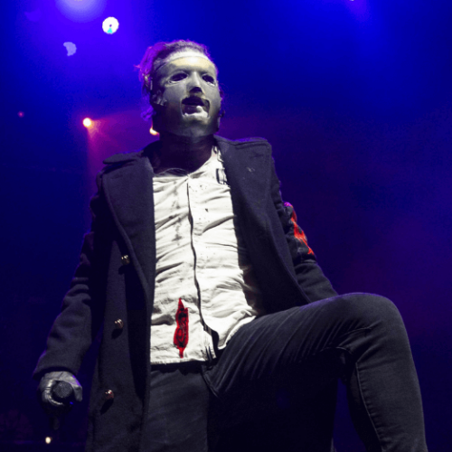 Image of Corey Taylor on stage wearing a costume mask and suit with a bloodstain