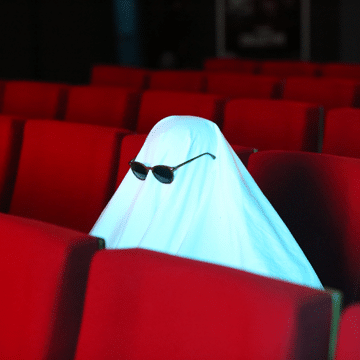 Sheet ghost wearing sunglasses sitting in movie theater