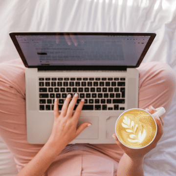 Laptop on top of crossed legs with hand holding cup of coffee