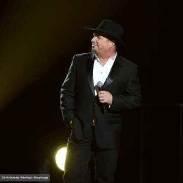 Photo of Garth Brooks in a black suit and black cowboy hat in front of a black background.