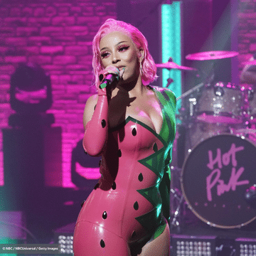 Doja Cat with pink hair singing in front of a drum kit