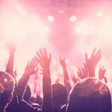 Photo shot from behind a crowd at a concert. The crowd has hands in the air.