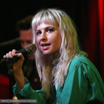 Photo of Paramore lead singer Hayley Williams with wavy blonde hair and a green top holding a microphone.