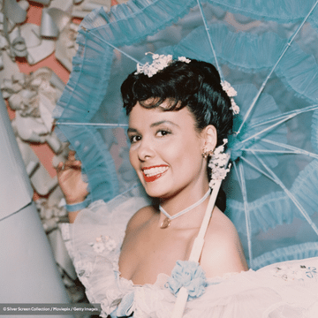 Photo of Lena Horne in a pink dress holding a teal umbrella and smiling.
