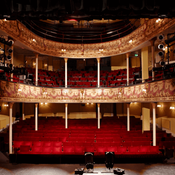 Stage view of theatre's interior, composed of rows of red theatre seats and upper seating sections