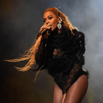 Photo of Beyonce wearing a black bodysuit in front of a dark background with white smoke behind her.