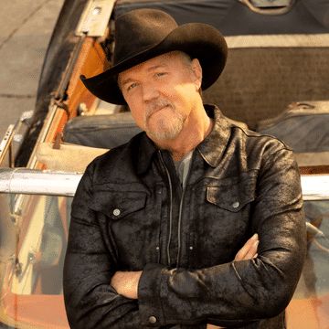 Photo of Trace Adkins in a black cowboy hat leaning against an orange convertible.