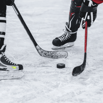Photo of two hockey players holding sticks on opposite sides of a puck.