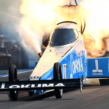 Photo of the Don Schumacher Racing Okuma car on a track with flames behind it.