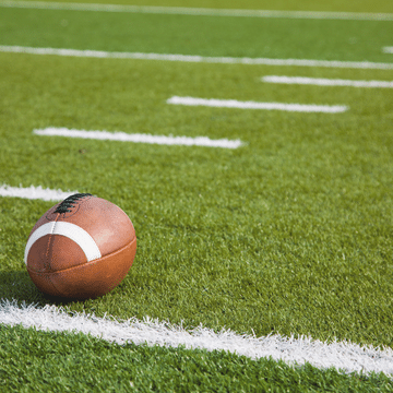 Photo of an American football sitting on a green football field painted with white lines.
