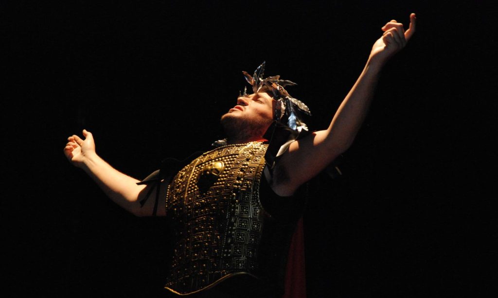 An actor stands with arms upraised.