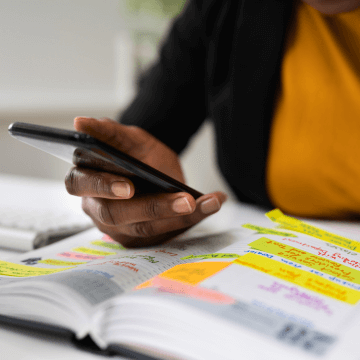 A woman looks through printed resources while shopping for tickets on her phone.