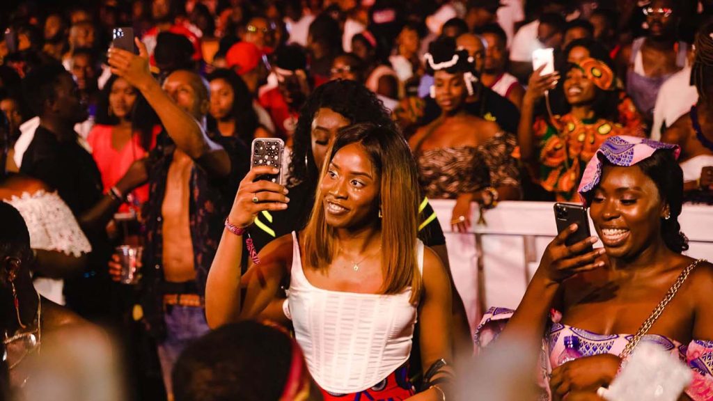 A young woman records a show with her phone surrounded by a large crowd.