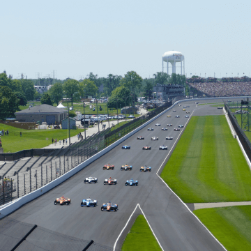 Photo of Indy cars in their signature three-row formation on the track at Indianapolis Motor Speedway.