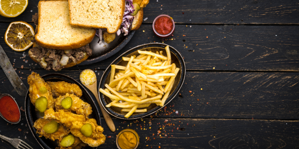 Imago of food like French fries, chicken tenders, spices, lemons and bread on plates against a black wooden surface
