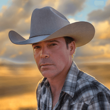 Clay Walker a clean shave man wearing a cowboy hat with a sunsetting in the background.