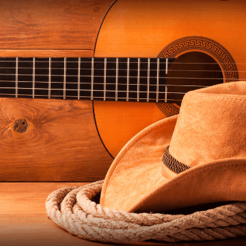 A cowboy hat on top of a coil of rope with a guitar in background representing country music and the Grand Ole Opry.