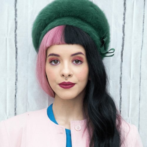 Picture of Melanie Martinez with pink and black split-dyed hair in a pink sweater and green fur beret