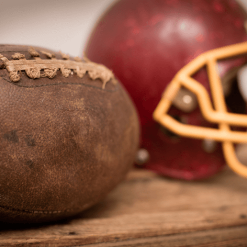 Photo of an old leather football sitting next to a red football helmet.