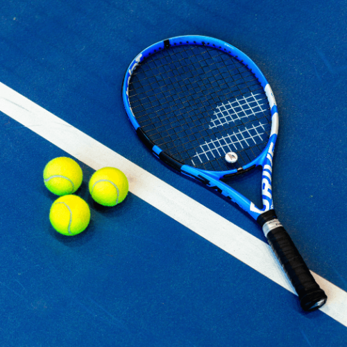 Photo of a racket and tennis balls on a blue tennis court.