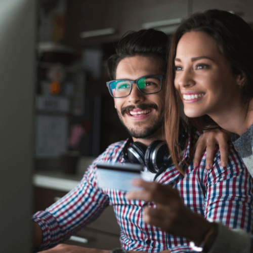 Photo of a man and woman looking at a computer screen. The man is also holding a credit card.