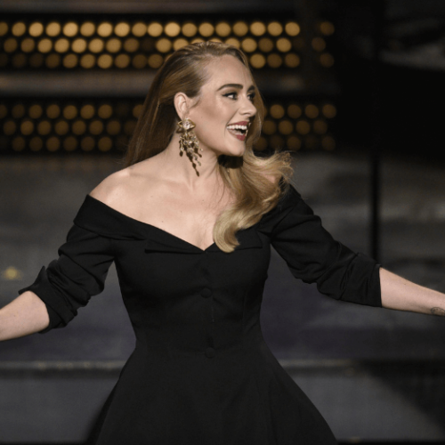 Image of Adele smiling on stage and wearing a black dress