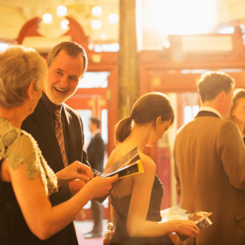 Image of people inside of a theatre holding playbills and socializing before a Broadway show.