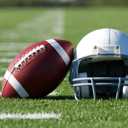Photo of a football and a helmet sitting on a grass football field.