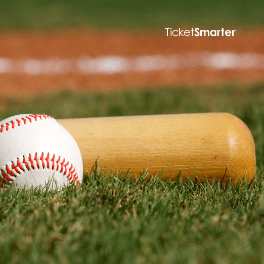 Photo of a baseball and bat sitting on grass. You can see infield dirt and the first base foul line behind them.